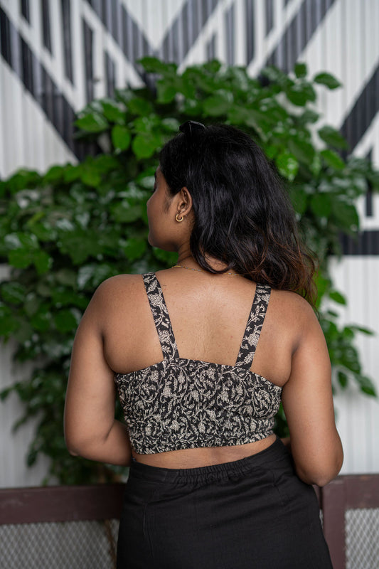 Woman wearing a patterned top and black skirt with plants and a geometric wall in the background
