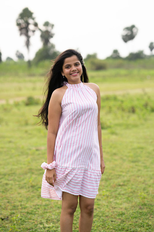 A woman wearing a pink and white striped halter-neck dress stands in a grassy outdoor field.