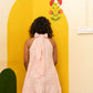 A woman viewed from behind wearing a pink and white striped halter dress with a large bow at the back, standing in front of a bright yellow painted wall with a floral motif.