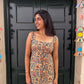 Woman wearing a patterned top standing in front of a black door with colorful decorations on a wall.