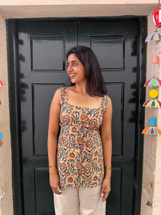 Woman wearing a patterned top standing in front of a black door with colorful decorations on a wall.