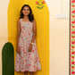 A woman stands wearing a sleeveless,  floral midi dress with thin straps. She is standing in a decorated room with a yellow arched wall, a green arch, and a wooden floor.