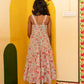 A woman stands with her back to the camera wearing a sleeveless, backless floral midi dress with thin straps. She is standing in a decorated room with a yellow arched wall, a green arch, and a wooden floor.