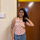 Woman posing in a room with a floral curtain and wooden door wearing pink shirt with floral patterns.