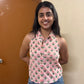 Woman wearing a pink floral top and blue jeans standing against a beige wall.
