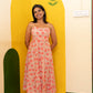 A woman stands barefoot indoors wearing a strapless midi dress with a pink and orange floral print on a light beige background. She is posed in front of a bright yellow painted arch on a cream wall.