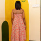 A woman stands with her back to the camera wearing a strapless pink floral midi dress, positioned in front of a yellow painted wall corner with a floral motif.