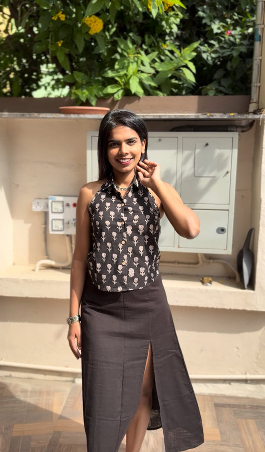 Woman wearing a black patterned top and dark skirt standing outdoors.