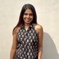 Woman wearing a black sleeveless top with white patterns against a beige wall