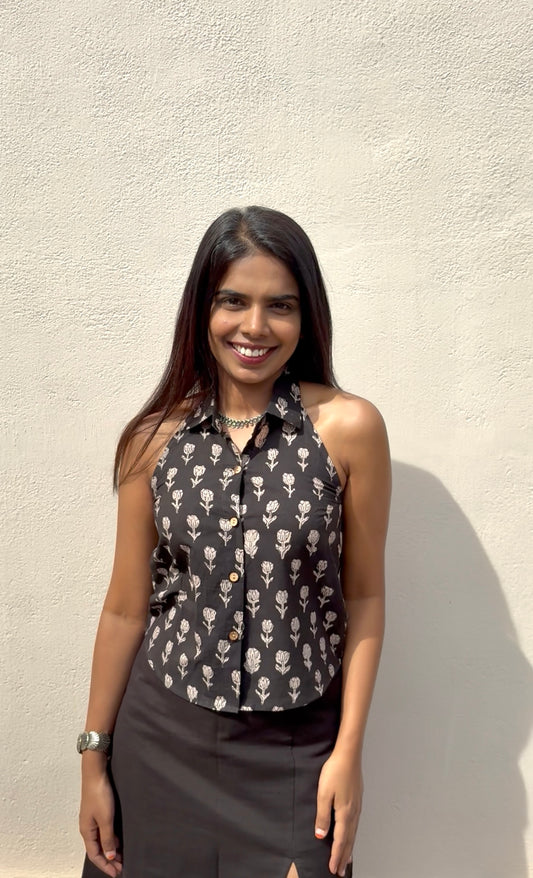 Woman wearing a black sleeveless top with white patterns against a beige wall