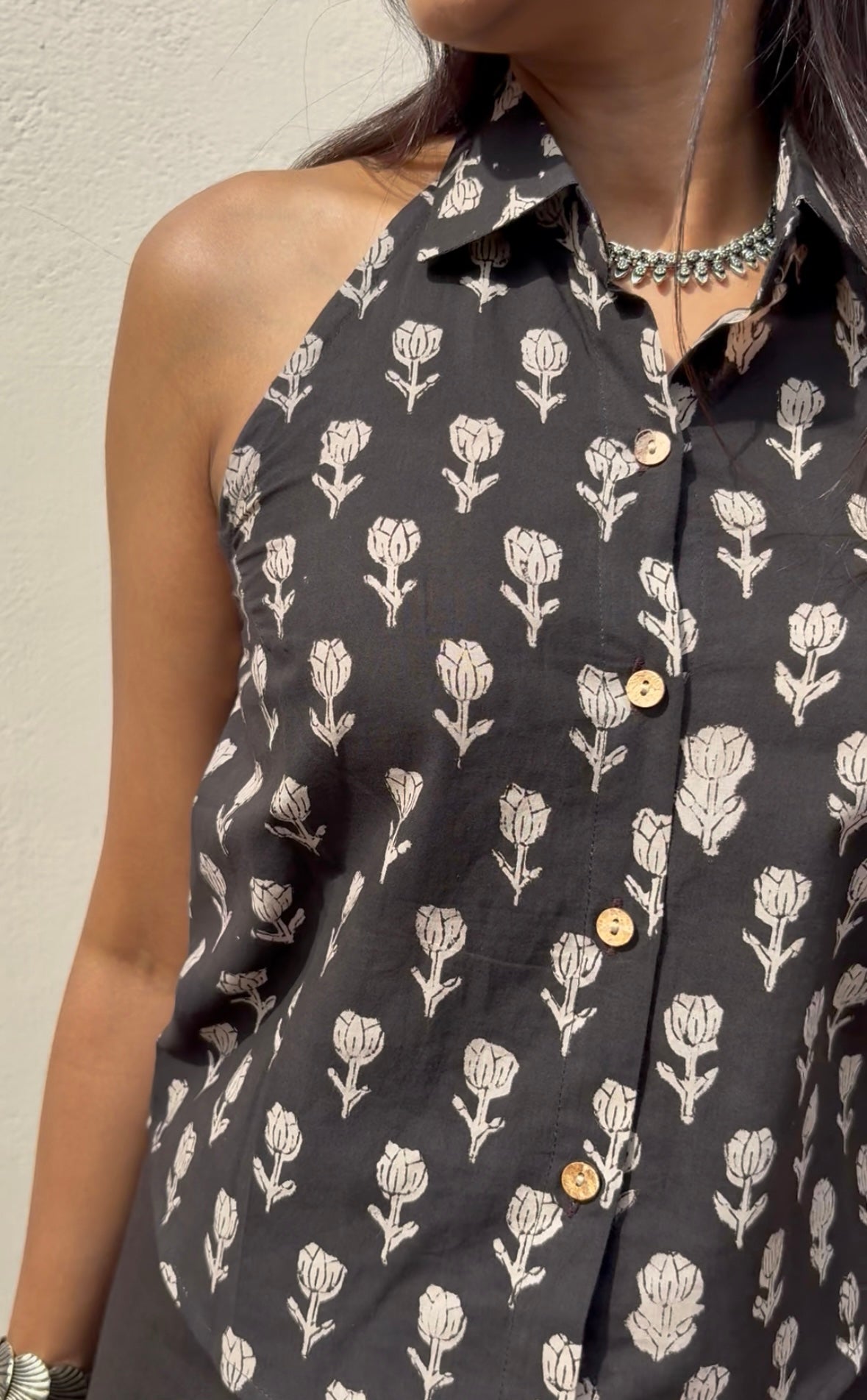 Black halter top with white floral pattern worn by a person against a neutral background