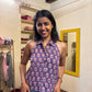 Woman in a purple floral top and blue jeans standing in front of a mirror.