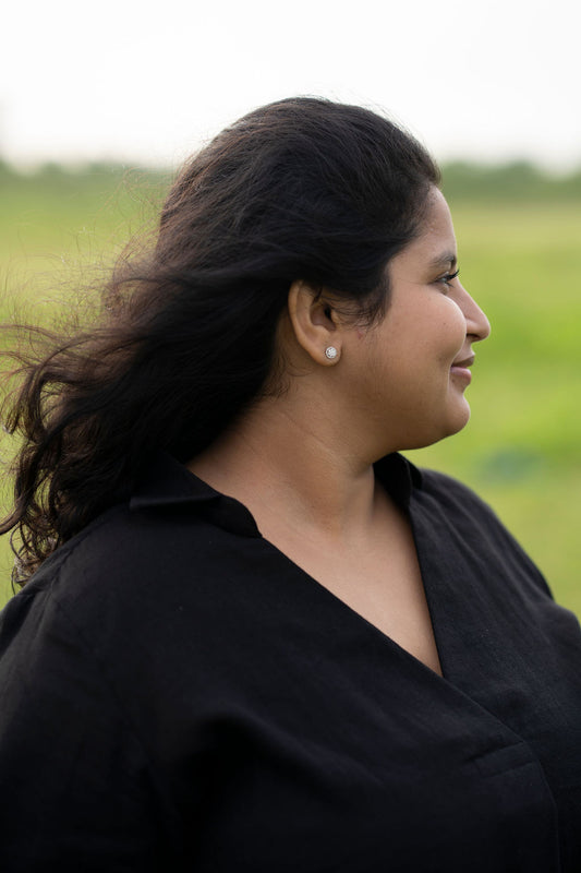 A woman in a black collared shirt shown in profile outdoors against a soft green blurred background.