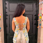 Woman wearing a floral top and beige pants standing in front of a black door.