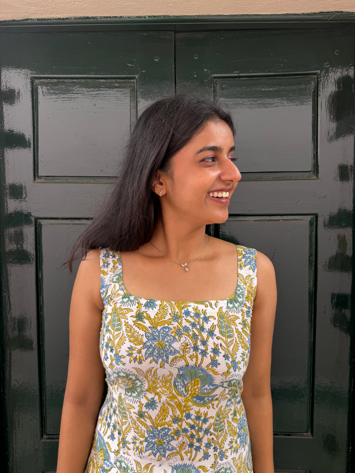 Woman wearing a floral dress standing in front of a dark green door.