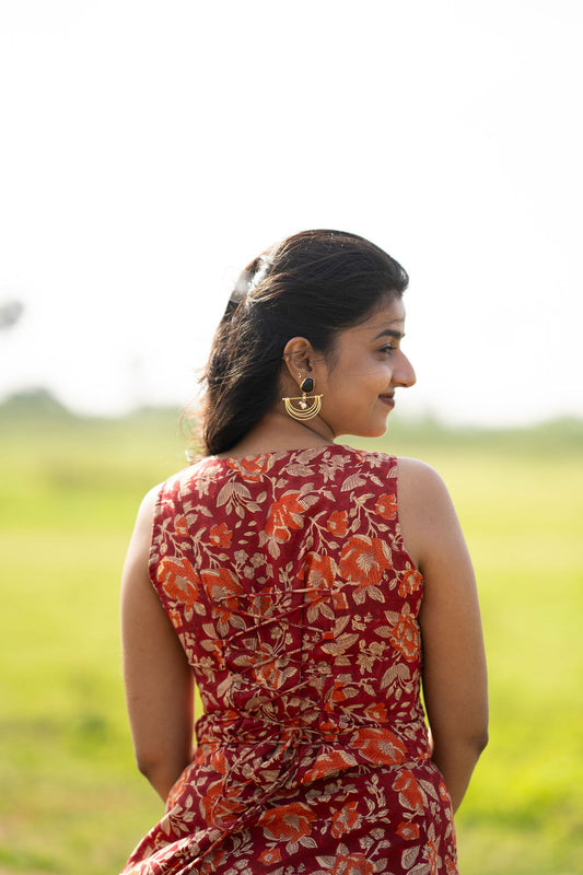A woman standing outdoors in a grassy field, shown from the back wearing a sleeveless red dress with an orange and beige floral pattern.