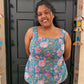 Woman wearing a floral top standing in front of a black door with decorative items on a beige wall.