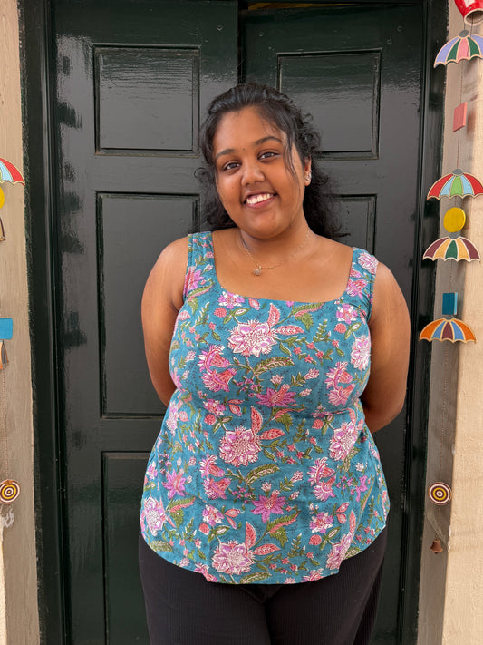 Woman wearing a floral top standing in front of a black door with decorative items on a beige wall.