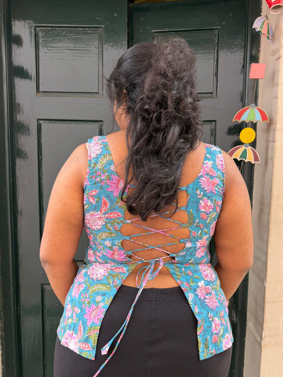 Person wearing a floral top with a back design, standing in front of a green door.