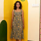 A woman stands barefoot in a colorful room wearing a sleeveless midi dress with a blue and gold floral block print pattern.